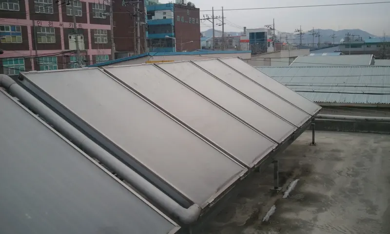옥상 난간 옆에 경사지게 설치된 평판형 태양열 집열기
